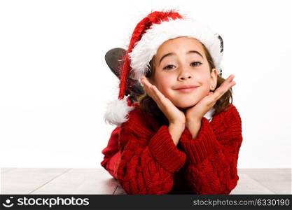 Adorable little girl wearing Santa hat laying on wooden floor on white background. Winter clothes
