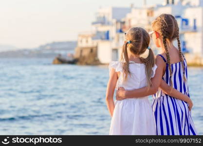 Adorable little girls at Little Venice the most popular tourist area on Mykonos island, Greece. Back view of beautiful kids look at Little Venice background.. Adorable little girl at Little Venice the most popular tourist area on Mykonos island, Greece.