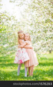 Adorable little girls in blooming cherry garden on beautiful spring day. Portrait of two kids outdoors. Adorable little girls in blooming apple tree garden on spring day