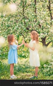 Adorable little girls in blooming cherry garden on beautiful spring day. Portrait of two kids outdoors. Adorable little girls in blooming apple tree garden on spring day