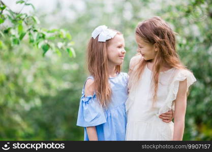 Adorable little girls in blooming cherry garden on beautiful spring day. Portrait of two kids outdoors. Adorable little girls in blooming apple tree garden on spring day