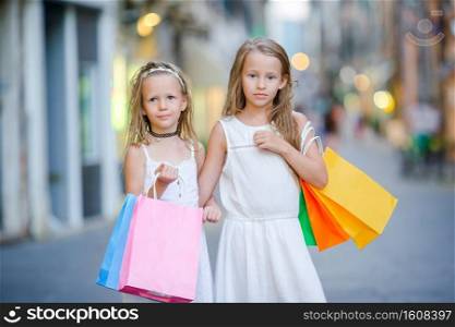 Adorable little girls on shopping. Portrait of kids with shopping bags in small italian town. Pretty smiling little girls with shopping bags