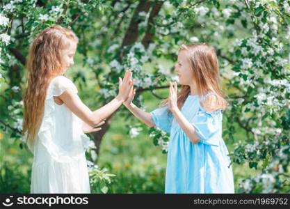 Adorable little girls on spring day playing together. Adorable little girls in blooming apple tree garden on spring day