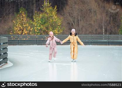 Adorable little girls skating on ice rink outdoors in winter snow day. Adorable girls skating on ice rink outdoors in winter snow day