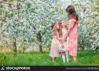 Adorable little girls with young mother in blooming garden on beautiful spring day. Adorable little girls with young mother in blooming cherry garden on beautiful spring day