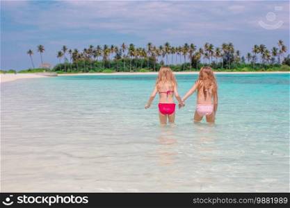Adorable little kids having fun on white beach in shallow water on Maldives. Adorable little girls at beach during summer vacation