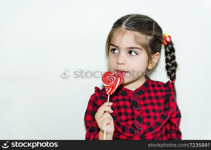 Adorable lovely little girl holds lollipop in heart shaped red candy.Holiday concept with isolated background.. Portrait of cute little happy girl in school uniform