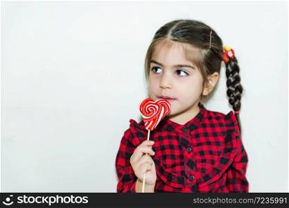 Adorable lovely little girl holds lollipop in heart shaped red candy.Holiday concept with isolated background.. Portrait of cute little happy girl in school uniform