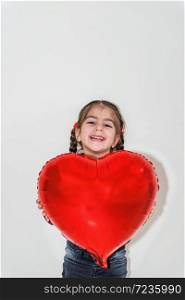 Adorable lovely little girl holds red heart shaped balloon.Holiday concept with isolated background. Portrait of cute little happy girl in school uniform