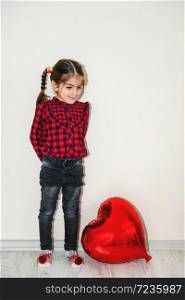 Adorable lovely little girl playing with red heart shaped balloon.Holiday concept with isolated background. Portrait of cute little happy girl in school uniform