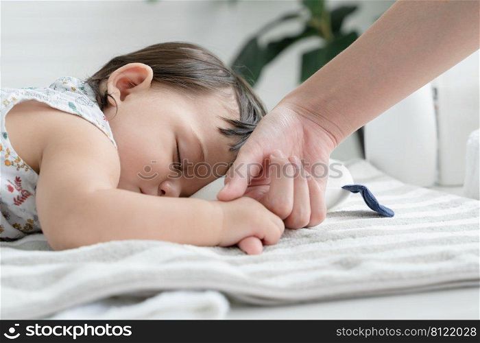 Adorable mixed race, Caucasian and Asian, little baby girl is sleeping and holding mother"s finger in her hand at bedroom at home. Selective focus on baby face. Purity and innocence concept