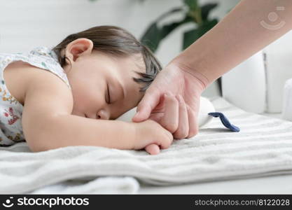 Adorable mixed race, Caucasian and Asian, little baby girl is sleeping and holding mother"s finger in her hand at bedroom at home. Selective focus on baby face. Purity and innocence concept