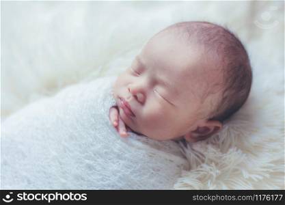 Adorable newborn baby sleeping in cozy room. Cute happy infant baby portrait with sleepy face in bed. Soft focus at the baby eyes. Newborn nursery care and baby lullaby concept.
