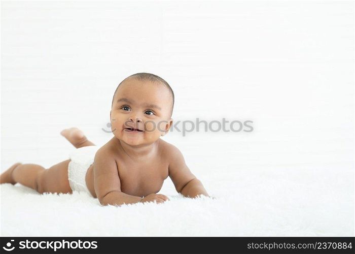 Adorable newborn Nigerian Asian baby girl wear diaper smiling with sparkling bright eyes and crawling on fluffy carpet on bed at home. White background. Copy space