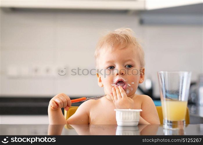 Adorable one year old baby boy eating yoghurt with spoon. Dirty messy face of toddler child.
