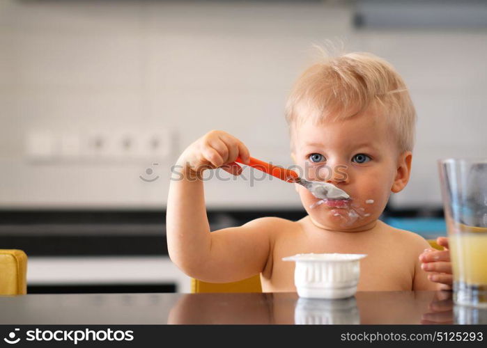 Adorable one year old baby boy eating yoghurt with spoon. Dirty messy face of toddler child.