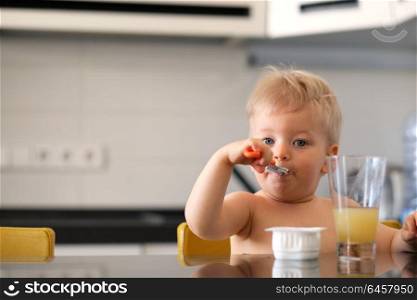 Adorable one year old baby boy eating yoghurt with spoon. Dirty messy face of toddler child.