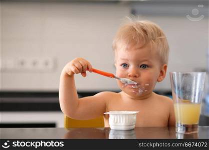 Adorable one year old baby boy eating yoghurt with spoon. Adorable one year old baby boy eating yoghurt with spoon. Dirty messy face of toddler child.