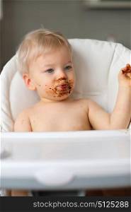 Adorable one year old baby boy playing with food. Toddler child eating fruit. Dirty messy face of happy kid.