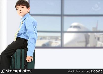 Adorable seven year old french american boy sitting on suitcase at airport.