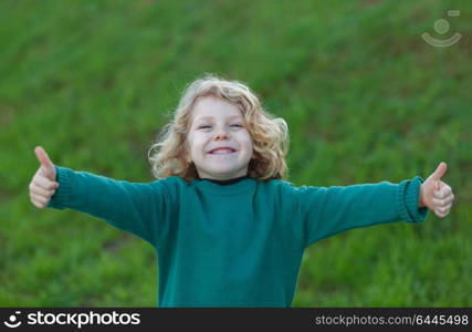 Adorable small blond child saying Ok in a park