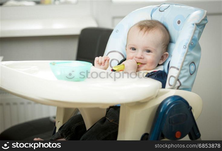 Adorable smiling baby boy eating porridge itself with spoon