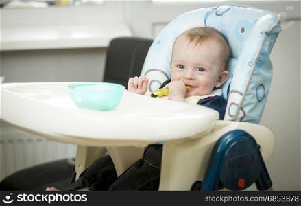 Adorable smiling baby boy eating porridge itself with spoon