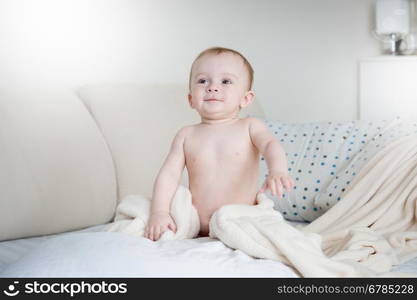 Adorable smiling baby boy in diapers sitting on bed with white sheets