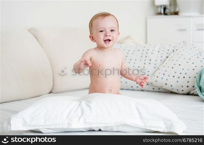 Adorable smiling baby boy playing on bed with big pillow
