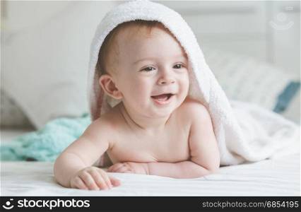 Adorable smiling baby in hooded towel lying on bed after having bathtime