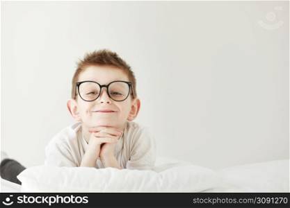 Adorable smiling child boy in glasses is lying in bed. morning dreaming on white bed. Adorable smiling child boy in glasses is lying in bed. morning dreaming on white bed.