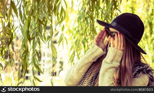 Adorable woman in sunglasses. Beauty and fashion of women. Young attractive fashionable girl wearing stylish hat waistcoat and sunglasses. Pretty woman around leaves of willow tree.