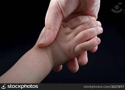 Adult and child hold hands in black background