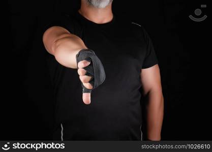 adult athlete in black uniform and hands rewound with textile bandage shows gesture dislike, low key