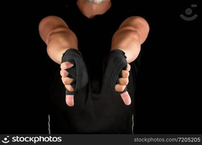 adult athlete in black uniform and hands rewound with textile bandage shows gesture dislike, low key