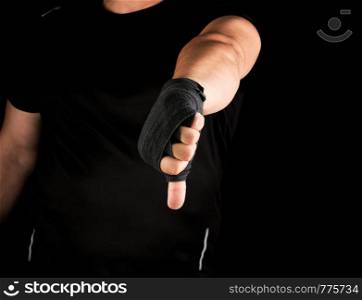 adult athlete in black uniform and hands rewound with textile bandage shows gesture dislike