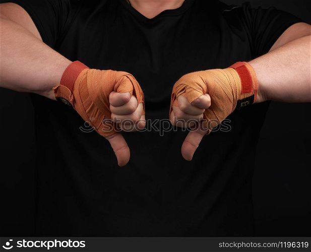 adult athlete in black uniform and hands rewound with textile orange bandage shows gesture dislike, low key