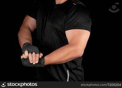 adult athlete in black uniform is standing in a rack with strained muscles, his hands are wrapped in a black textile bandage, dark background