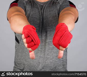 adult athlete in gray uniform and hands rewound with textile red bandage shows gesture dislike, white background