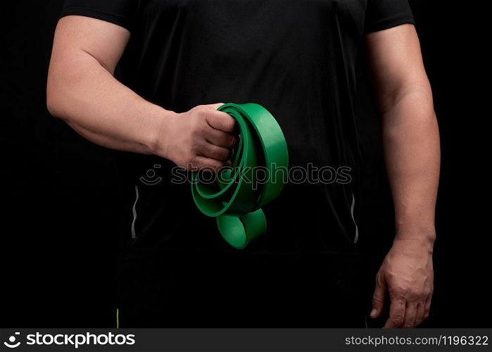 adult athlete with a muscular body in black clothes is doing physical exercises with sport green rubber, low key. Healthy active lifestyle