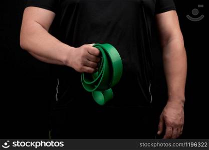 adult athlete with a muscular body in black clothes is doing physical exercises with sport green rubber, low key. Healthy active lifestyle