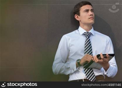 Adult businessman using tablet computer outdoors leaning on wall of office building
