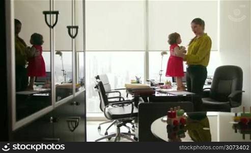 Adult businesswoman with little baby in office. The multitasking mom plays with her child standing on desk