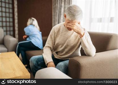 Adult couple at home, family quarrel or conflict. Mature husband and wife sitting on couch with their backs to each other, problems in relationship