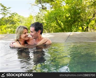 Adult couple embracing in pool smiling