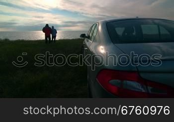 Adult couple near parked car enjoying view of the sea coast at sunset