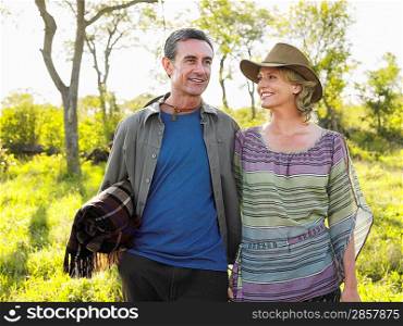 Adult couple outdoors man carrying blanket woman wearing hat smiling