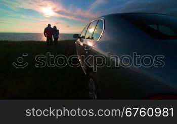 Adult couple silhouette near his car enjoying view of the sea coast at sunset