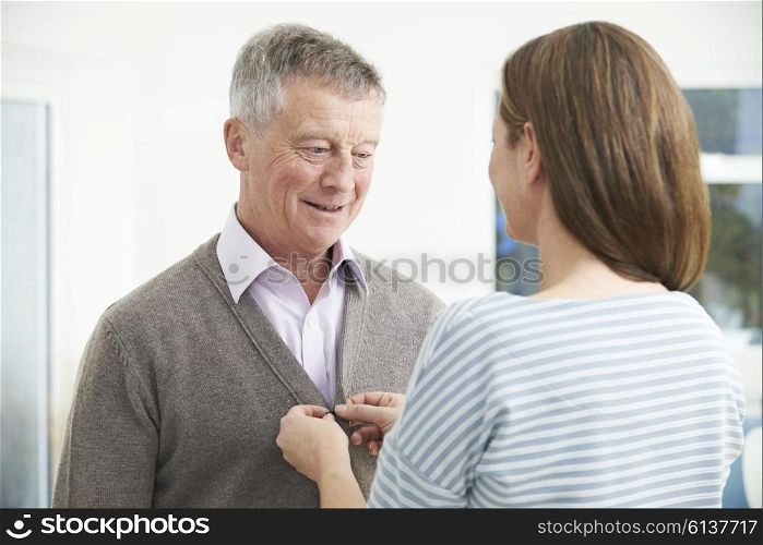 Adult Daughter Helping Senior Man To Button Cardigan