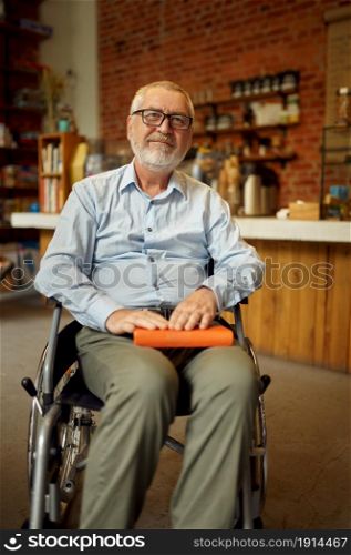 Adult disabled man in wheelchair holds a book, disability, bookshelf and university library interior on background. Handicapped older male person, paralyzed people get knowledge. Adult disabled man in wheelchair holds a book